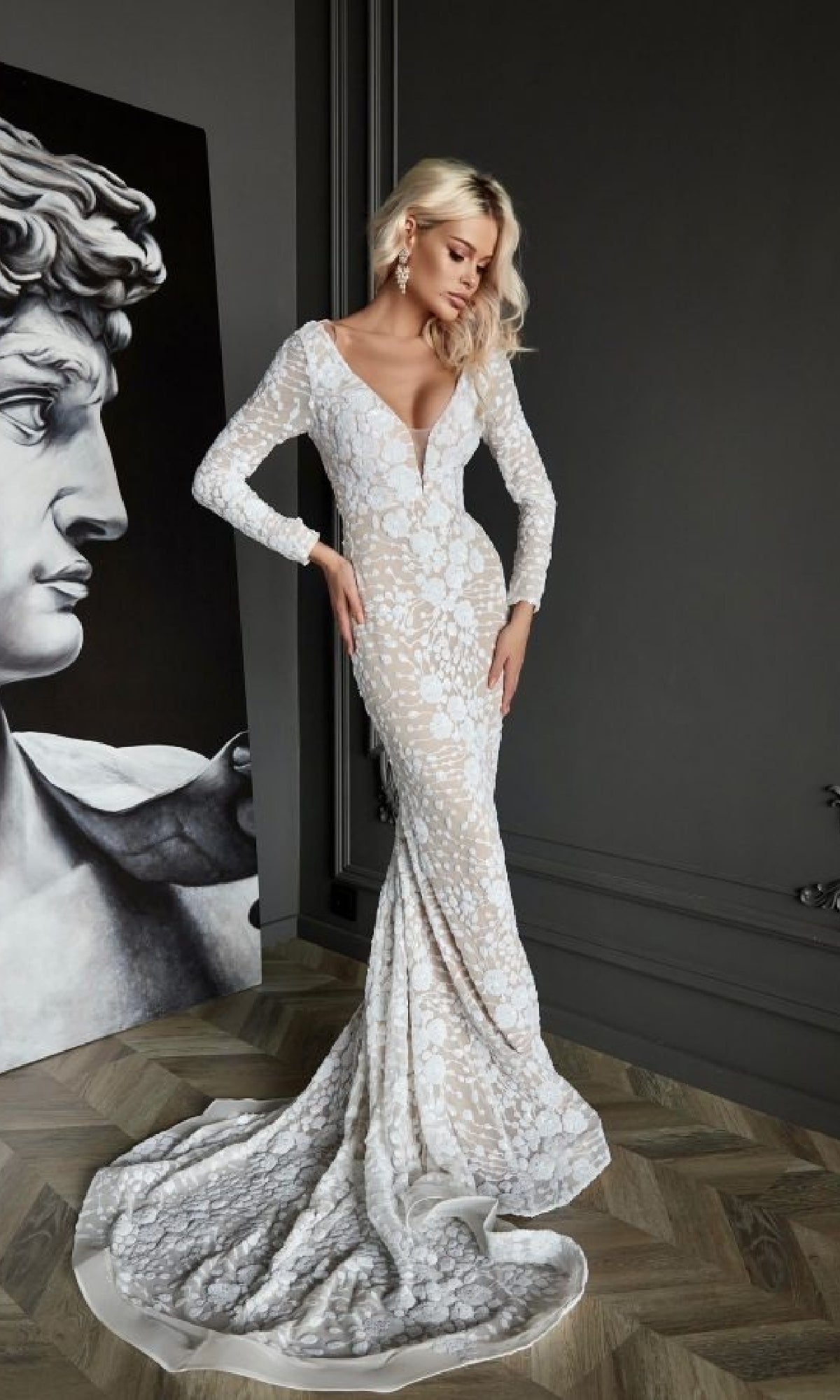 A woman wearing the Tina Holly BB023 long formal dress stands indoors near a large sculpture of a classical male bust.